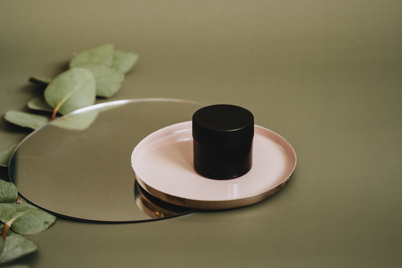 services-03 A minimalist display of a skincare product on a tray with eucalyptus leaves on a reflective surface.