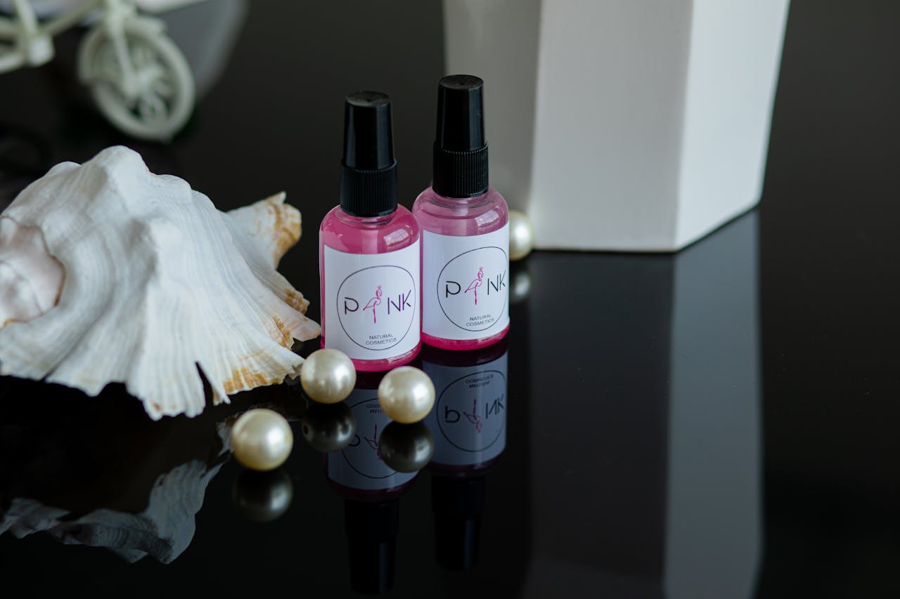 services-01 A stylish still life scene featuring pink cosmetic bottles, a white shell, and pearls.